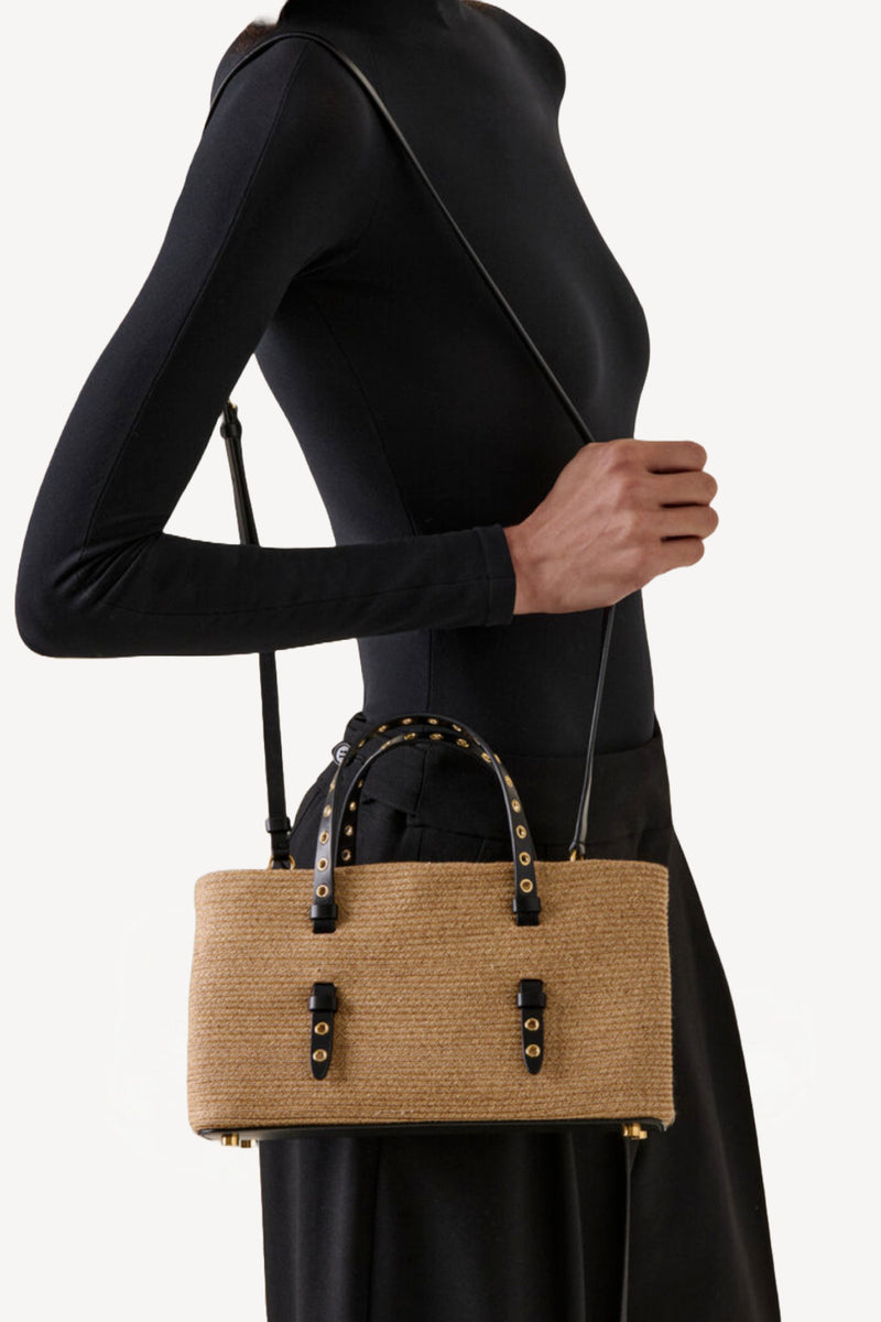 Front view of natural straw bag on model wearing a black short and black skirt on white background.