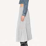 Side view of gris souris pleated skirt on model wearing jean jacket and boots, against a white background.
