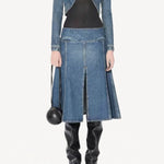 Front view of denim slit skirt on model wearing denim jacket, black bodysuit and boots, against a white background.