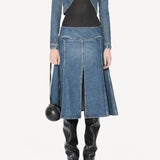 Front view of denim slit skirt on model wearing denim jacket, black bodysuit and boots, against a white background.