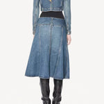 Back view of denim slit skirt on model wearing denim jacket, black bodysuit and boots, against a white background.