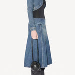 Side view of denim slit skirt on model wearing denim jacket, black bodysuit and boots, against a white background.