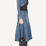 Side view of denim slit skirt on model wearing denim jacket, black bodysuit and boots, against a white background.