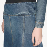 Side closeup of denim slit skirt on model wearing black bodysuit and denim jacket, against a white background.
