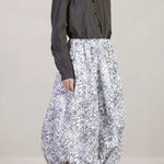 Side view of bright flower carla skirt on model wearing dark grey top with black oxfords, against white background.