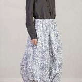 Side view of bright flower carla skirt on model wearing dark grey top with black oxfords, against white background.