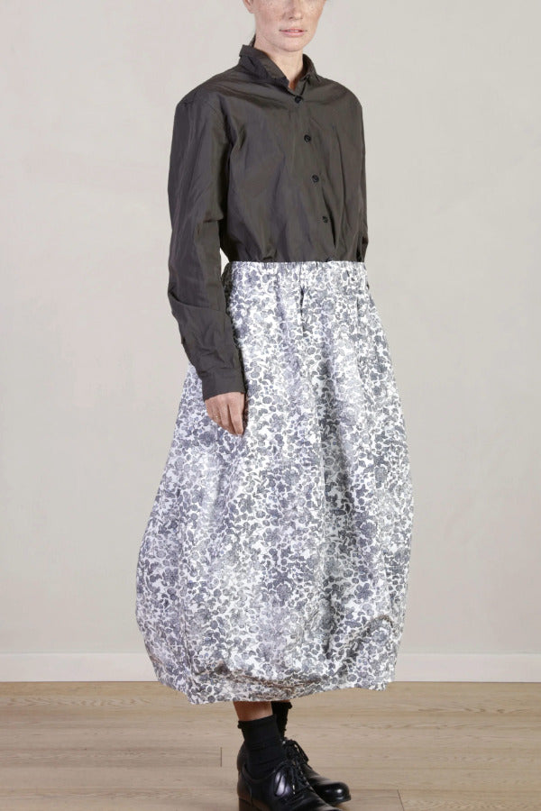 Side view of bright flower carla skirt on model wearing dark grey top with black oxfords, against white background.