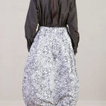 Back view of bright flower carla skirt on model wearing dark grey top with black oxfords, against a white background.
