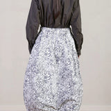 Back view of bright flower carla skirt on model wearing dark grey top with black oxfords, against a white background.