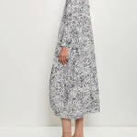 Side view of bright flower letty dress on model wearing white loafers, against a white background.