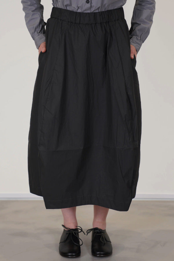 Front alternate view of carbon carla skirt on model wearing dark grey top and black oxfords, against a white background.