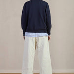 Back view of stone Chloe pants on model wearing stripe shirt, navy sweater and black oxfords, against a white background.