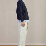 Side view of stone Chloe pants on model wearing stripe shirt, navy sweater and black oxfords, against a white background.
