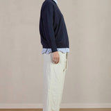 Side view of stone Chloe pants on model wearing stripe shirt, navy sweater and black oxfords, against a white background.