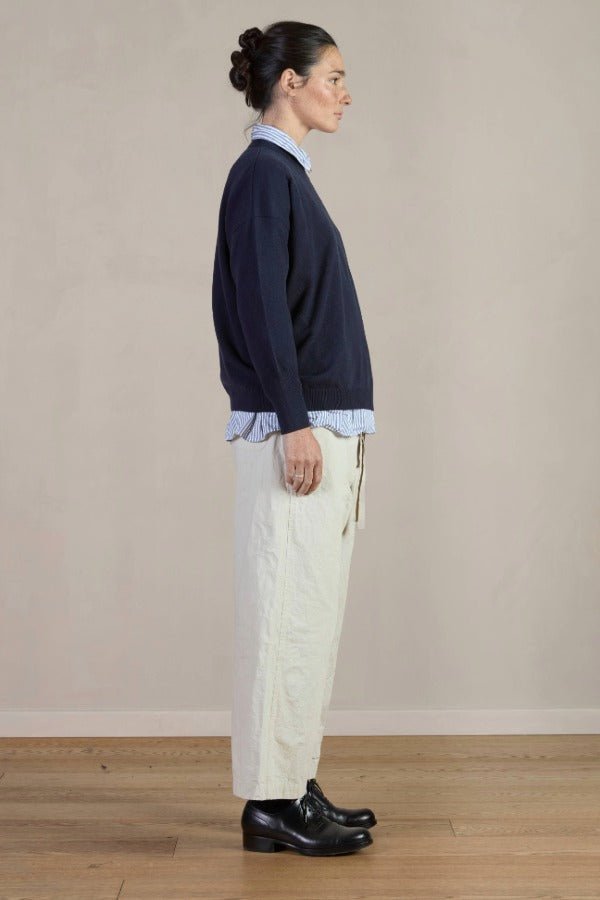 Side view of stone Chloe pants on model wearing stripe shirt, navy sweater and black oxfords, against a white background.