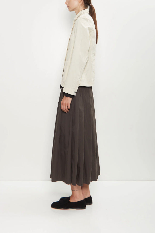 Side view of stone caryl jacket on model wearing brown skirt and black loafers, against a white background.