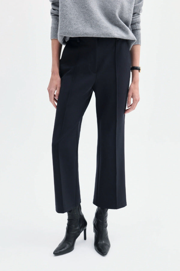Front closeup view of black cropped flared pant on model wearing grey sweater and black boots, against a white background.