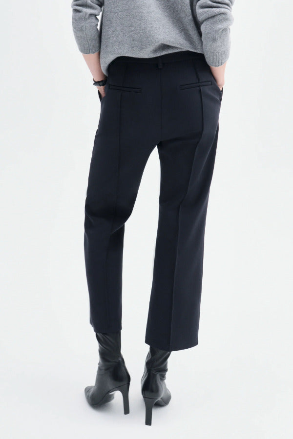 Back view of black cropped flared pant on model wearing grey sweater and black boots, against a white background.