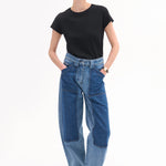 Front view of indigo denim patchwork pants on model wearing black t-shirt and black sandals, against white background.
