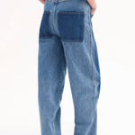 Back view of indigo denim patchwork pants on model wearing black t-shirt and black sandals, against white background.