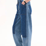 Side view of indigo denim patchwork pants on model wearing black t-shirt and black sandals, against white background.