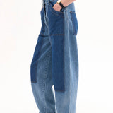 Side view of indigo denim patchwork pants on model wearing black t-shirt and black sandals, against white background.