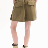 Back view of olive combat shorts on model wearing a dark green tank top and leather wrap sandals on white background.