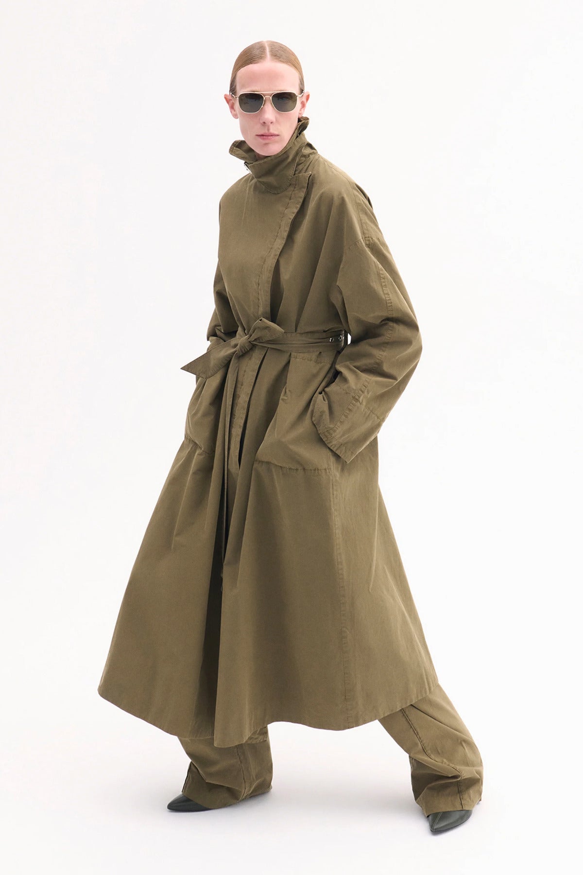Front slanted view of olive oversized trench coat on model wearing olive pants and black pointed toe heels, against white background.