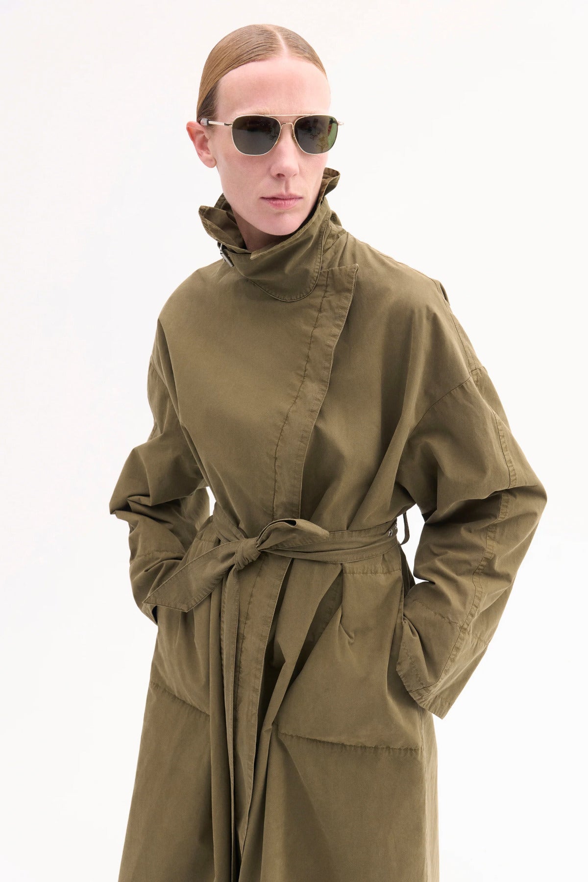 Front closeup view of olive oversized trench coat on model wearing sunglasses, against white background.