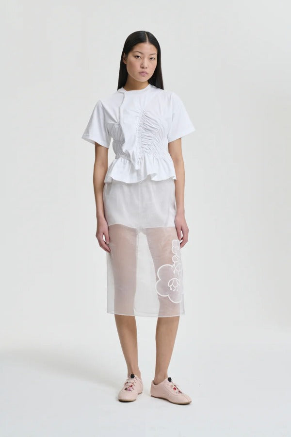 Front view of white ace t-shirt on model wearing white shorts and pink sneakers, against a white background.