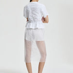 Back view of white ace t-shirt on model wearing white shorts and pink sneakers, against a white background.