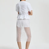 Back view of white ace t-shirt on model wearing white shorts and pink sneakers, against a white background.