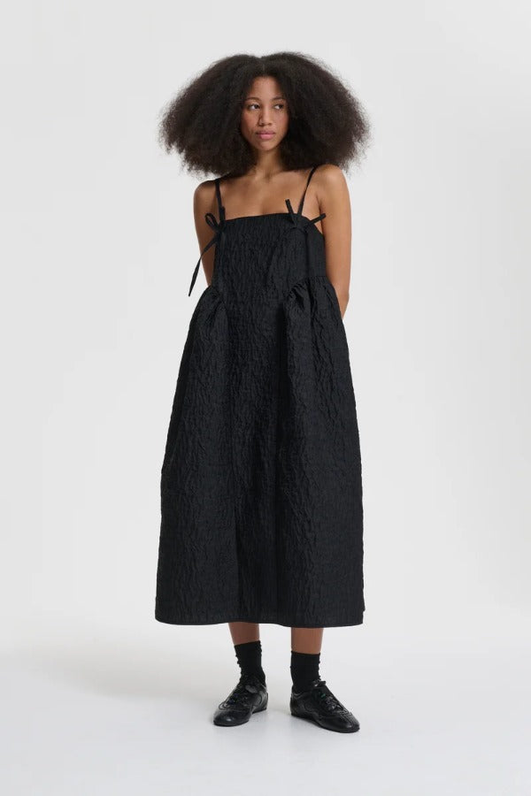 Front view of black ambra dress on model wearing black sneakers, against a white background.