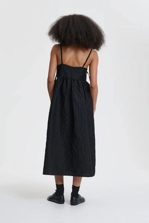 Back view of black ambra dress on model wearing black sneakers, against a white background.