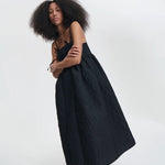 Side view of black ambra dress on model wearing black sneakers, against a white background.
