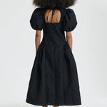 Back view of black bali dress on model wearing black sneakers and socks, against a white background.