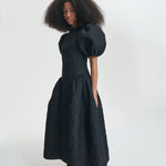 Side view of black bali dress on model wearing black sneakers and socks, against a white background.