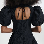 Back closeup view of black bali dress on model, against a white background.