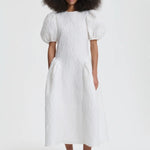 Front view of white bali dress on model wearing black flats, against a white background.