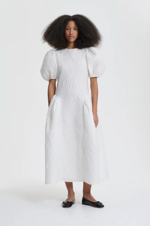 Front view of white bali dress on model wearing black flats, against a white background.