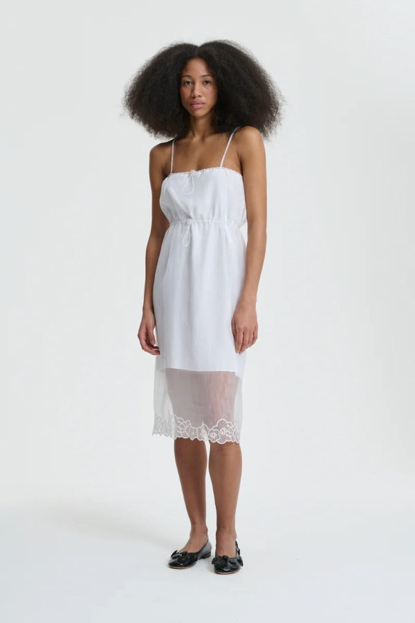 Front view of white barr dress on model wearing black flats, against a white background.