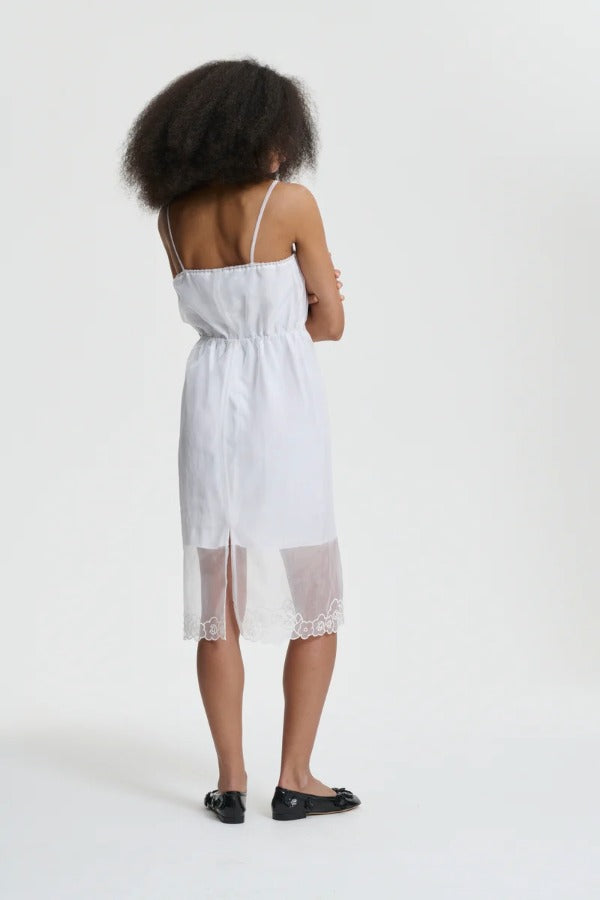 Back view of white barr dress on model wearing black flats, against a white background.