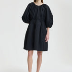 Front view of black birgitte dress on model wearing black flats, against a white background.