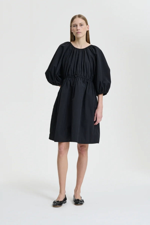 Front view of black birgitte dress on model wearing black flats, against a white background.