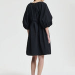 Back view of black birgitte dress on model wearing black flats, against a white background.