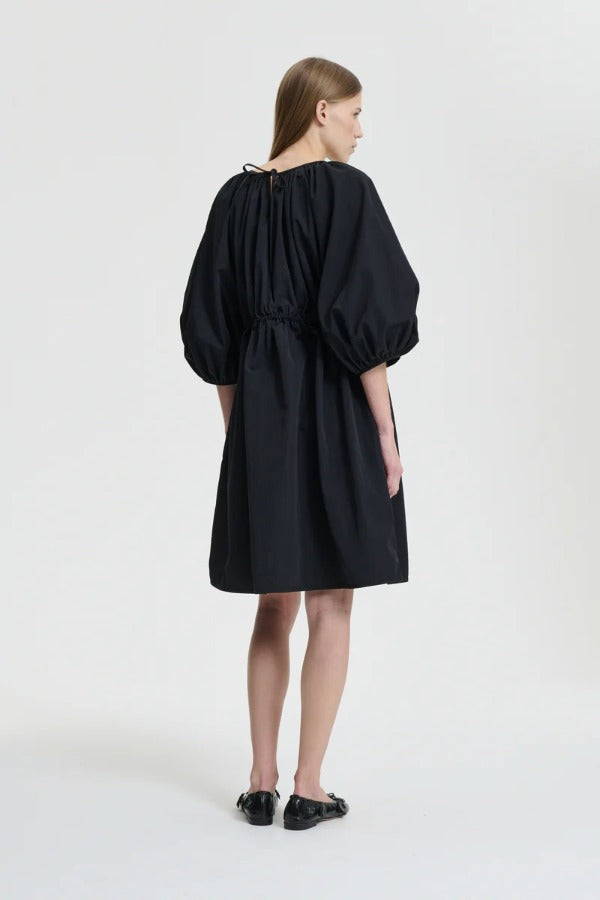 Back view of black birgitte dress on model wearing black flats, against a white background.
