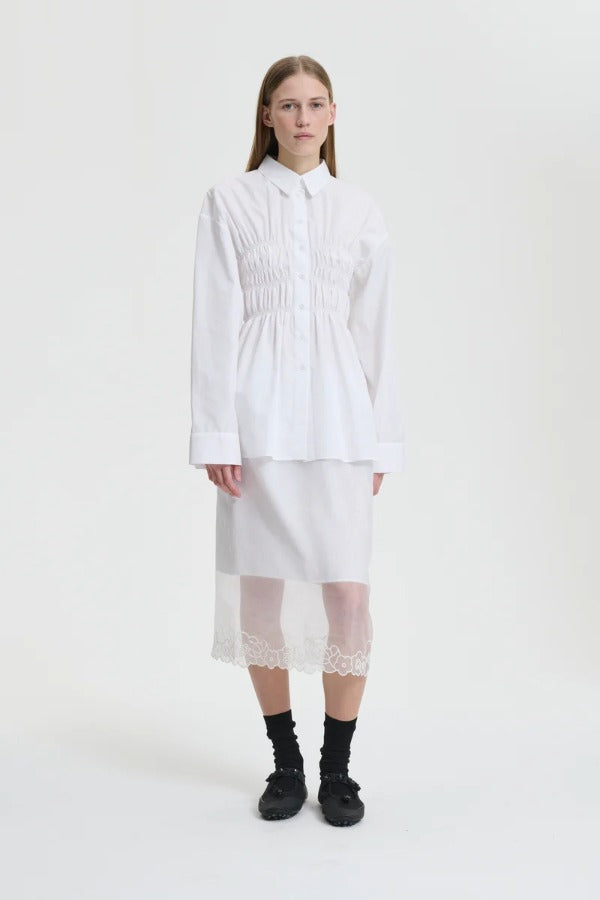 Front view of white braxton shirt on model wearing white slip and black sneakers, against a white background.