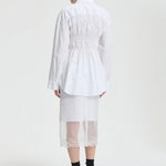 Back view of white braxton shirt on model wearing white slip and black sneakers, against a white background.