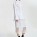 Side view of white braxton shirt on model wearing white slip and black sneakers, against a white background.