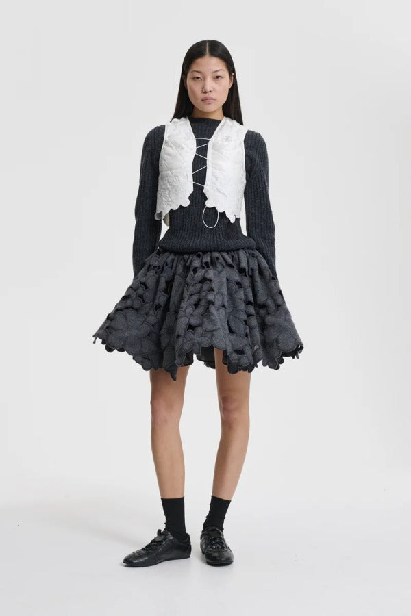 Front view of snow white breno vest on model wearing black dress and sneakers, against a white background.